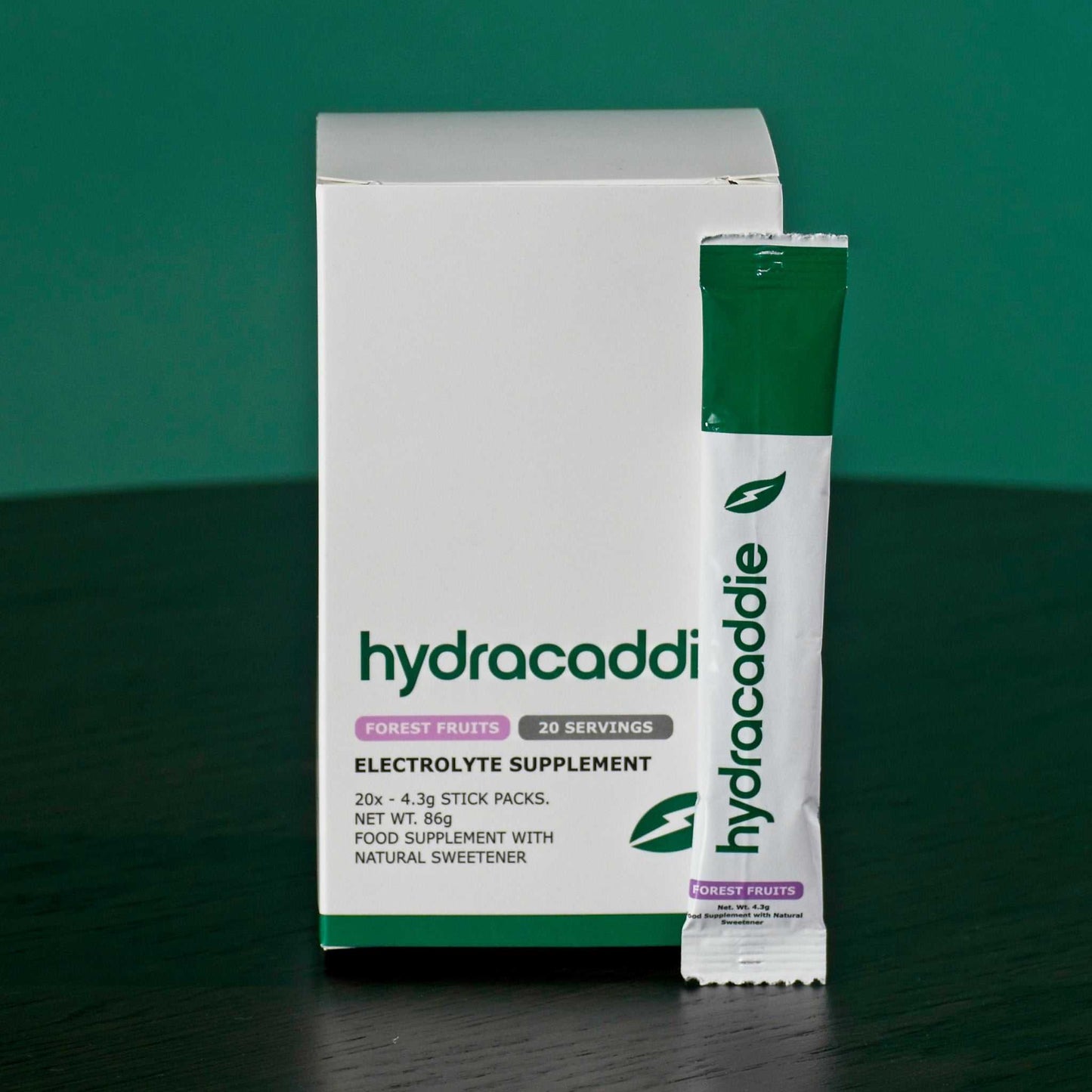 Box of hydracaddie forest fruits electrolyte supplement on a green background with a single stick sachet next to the box.