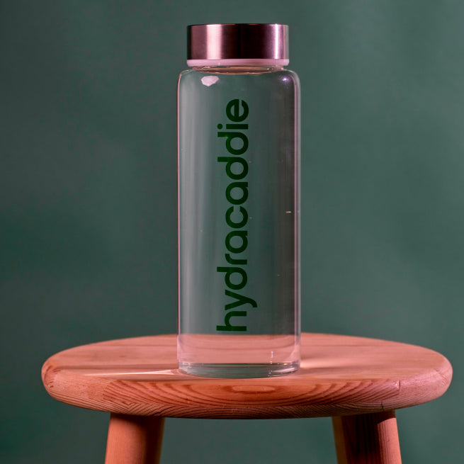 Product image for the hydracaddie lifestyle bottle. A premium glass bottle with stainless steel lid on a green background.