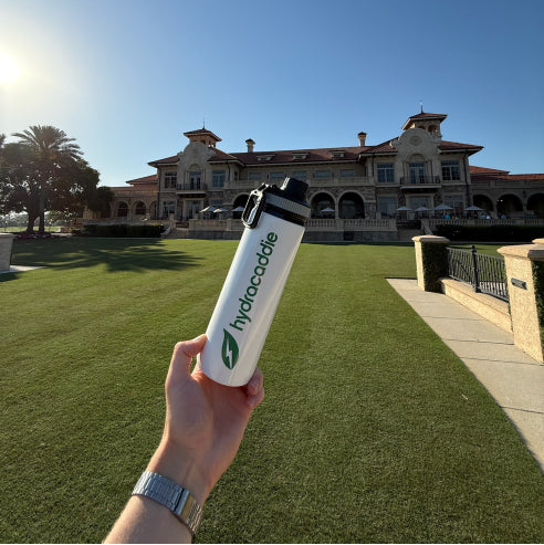 hydracaddie water bottle held in front of TPC sawgrass clubhouse on a sunny day