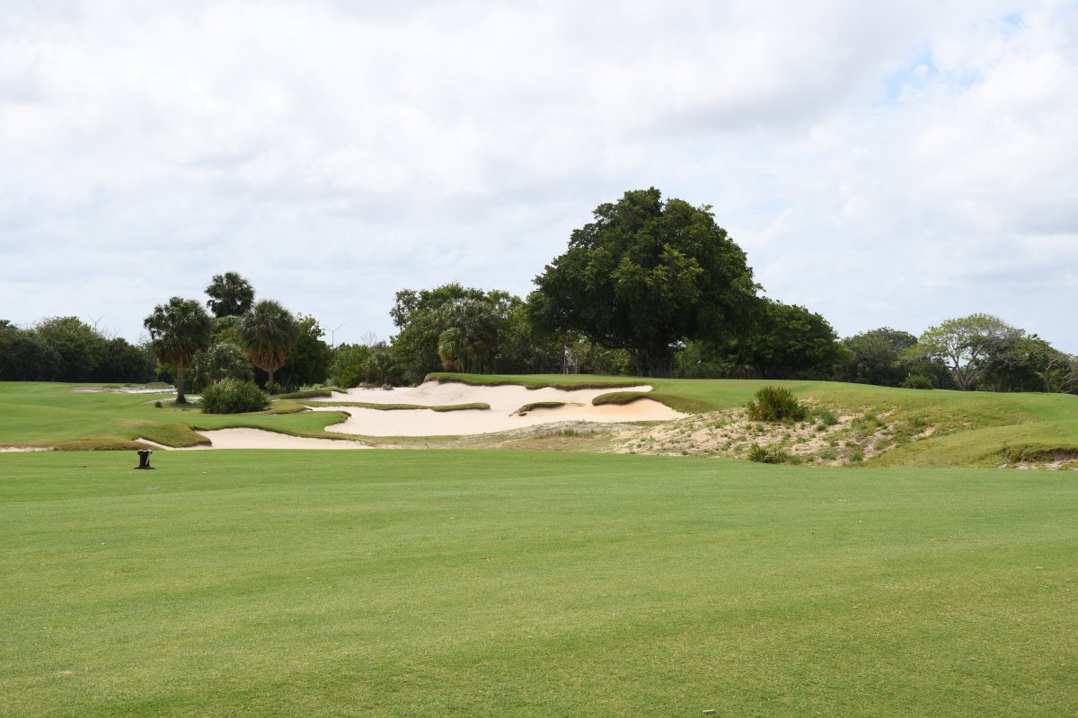Golf course with green grass, sand bunkers, and trees under a cloudy sky.