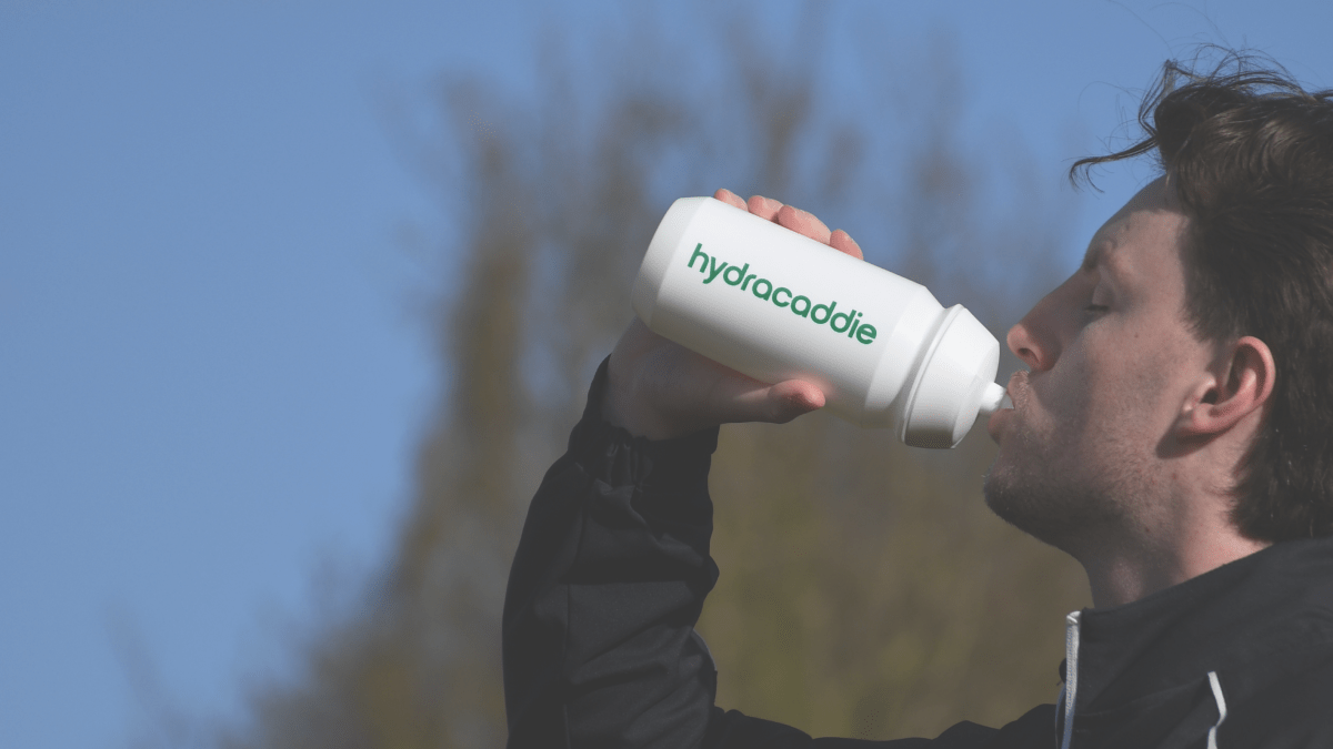 Person drinking from a 'hydracaddie' water bottle against a blue sky background